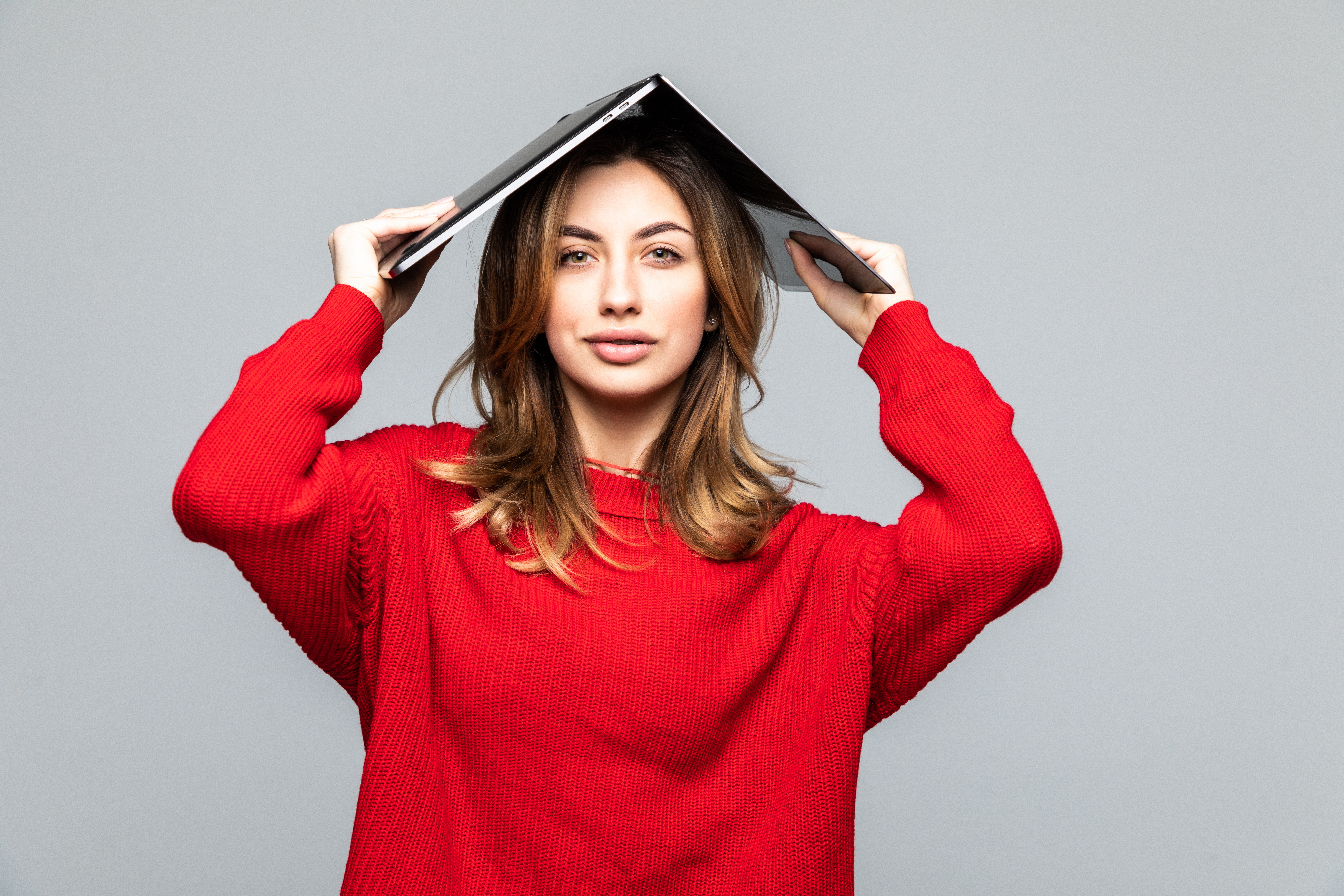 happy-woman-red-sweater-holding-laptop-her-head-like-roof-gray-wall